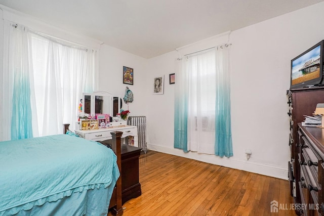 bedroom featuring radiator heating unit, light wood-type flooring, and baseboards