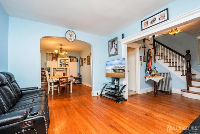 living room with arched walkways, wood finished floors, stairs, radiator heating unit, and an inviting chandelier