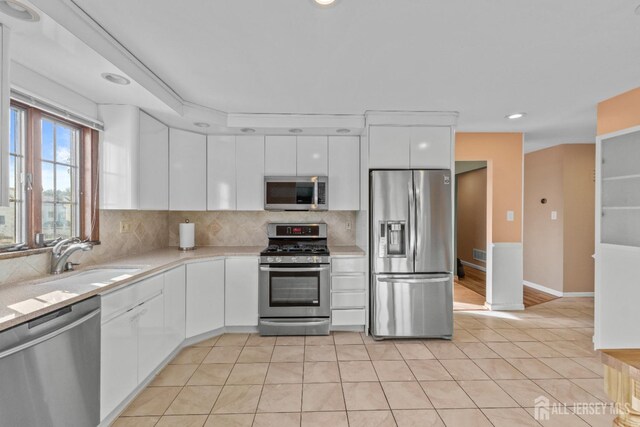 kitchen with tasteful backsplash, sink, white cabinets, light tile patterned floors, and stainless steel appliances