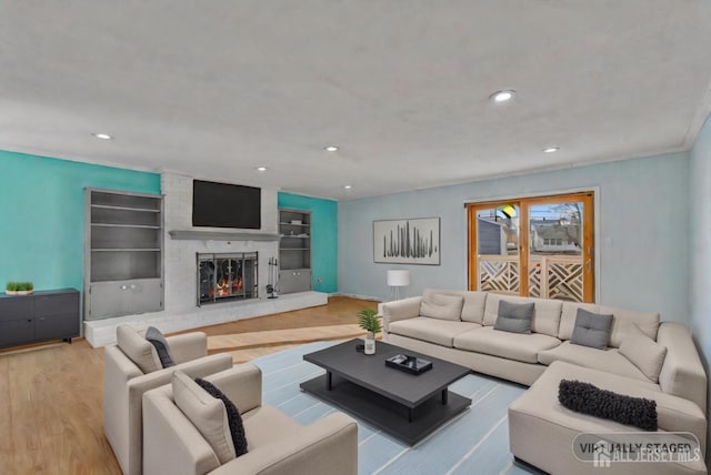 living room with ornamental molding, built in features, a fireplace, and light hardwood / wood-style floors