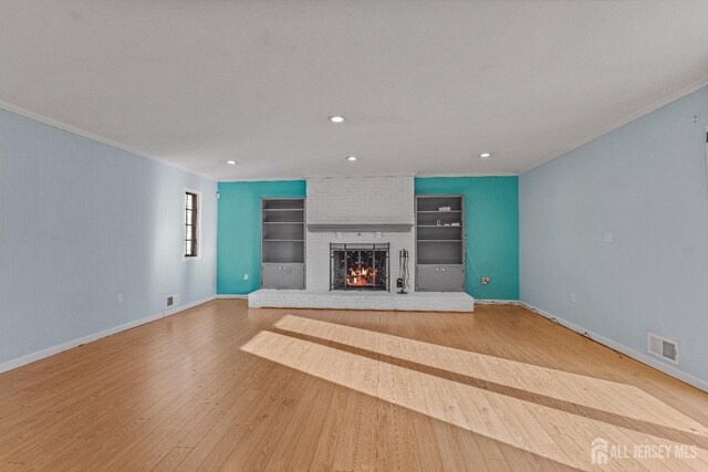 unfurnished living room with crown molding, a brick fireplace, built in features, and light hardwood / wood-style flooring