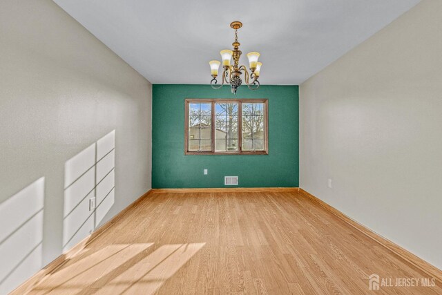 unfurnished room featuring an inviting chandelier and light hardwood / wood-style flooring