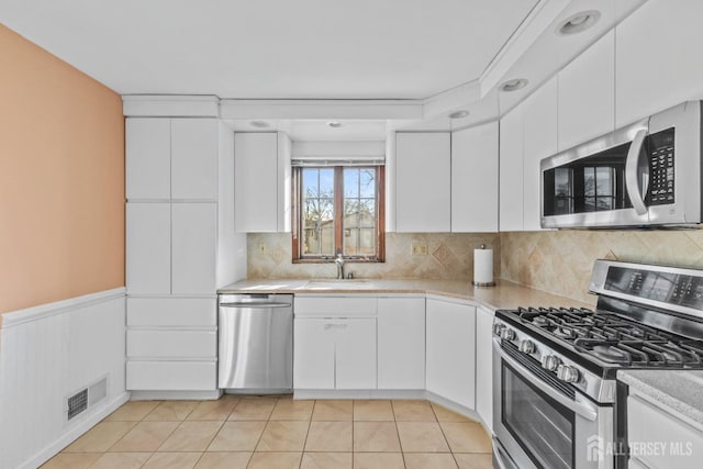 kitchen with white cabinetry, stainless steel appliances, backsplash, and light tile patterned floors