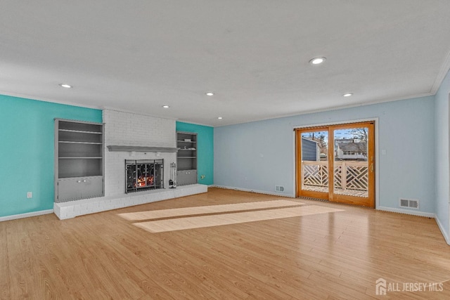 unfurnished living room with built in shelves, crown molding, a brick fireplace, and light hardwood / wood-style flooring