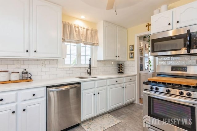 kitchen featuring ceiling fan, appliances with stainless steel finishes, sink, white cabinets, and tasteful backsplash