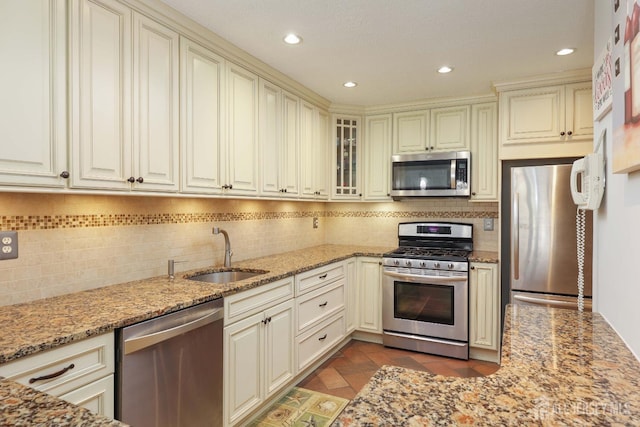 kitchen featuring appliances with stainless steel finishes, a sink, cream cabinets, light stone counters, and recessed lighting