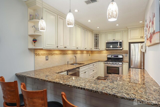 kitchen with appliances with stainless steel finishes, a sink, light stone counters, cream cabinetry, and recessed lighting