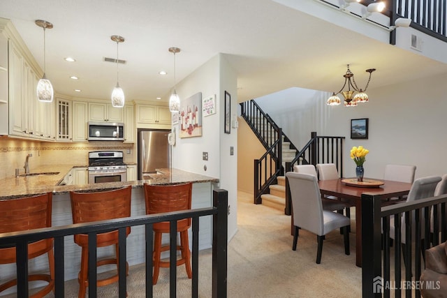 kitchen featuring cream cabinetry, stainless steel appliances, a sink, stone counters, and decorative backsplash
