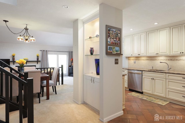 kitchen featuring stainless steel dishwasher, a sink, a chandelier, backsplash, and cream cabinetry