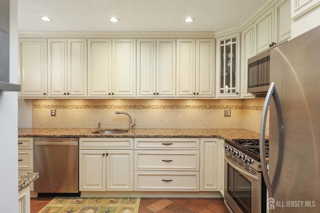 kitchen with appliances with stainless steel finishes, a sink, cream cabinets, light stone counters, and recessed lighting