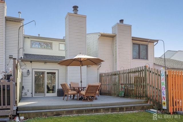 rear view of house featuring a chimney, fence, and a wooden deck