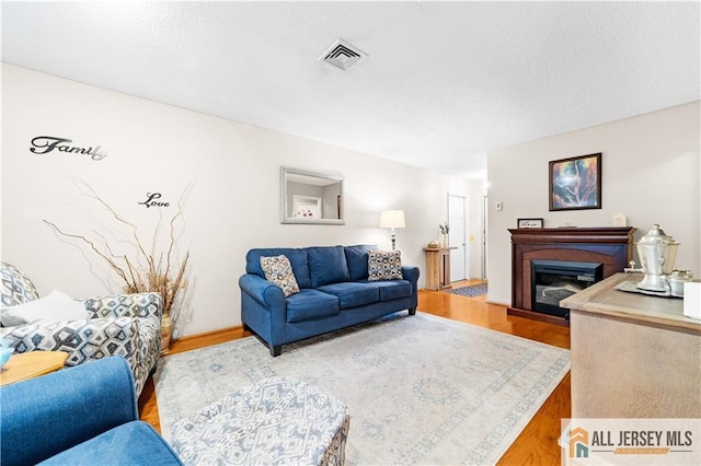 living room featuring wood finished floors, a glass covered fireplace, and a textured ceiling