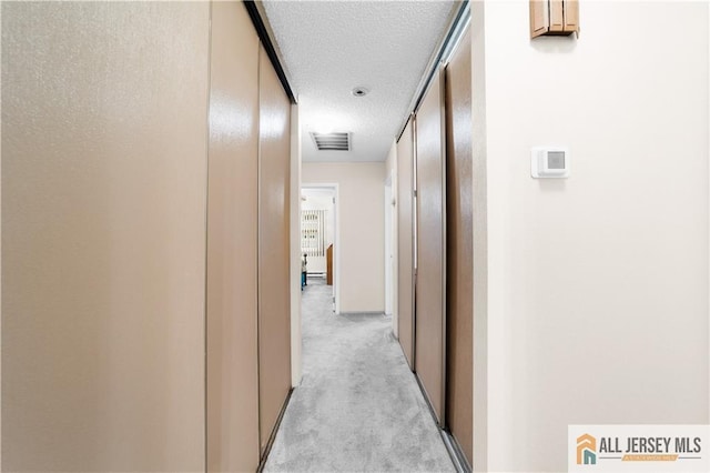 corridor featuring a textured ceiling, light carpet, and baseboards