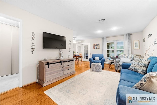 living area with light wood-style floors, a baseboard radiator, ceiling fan, and baseboards