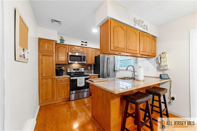 kitchen with stainless steel appliances, a sink, a peninsula, light wood-style floors, and a breakfast bar area