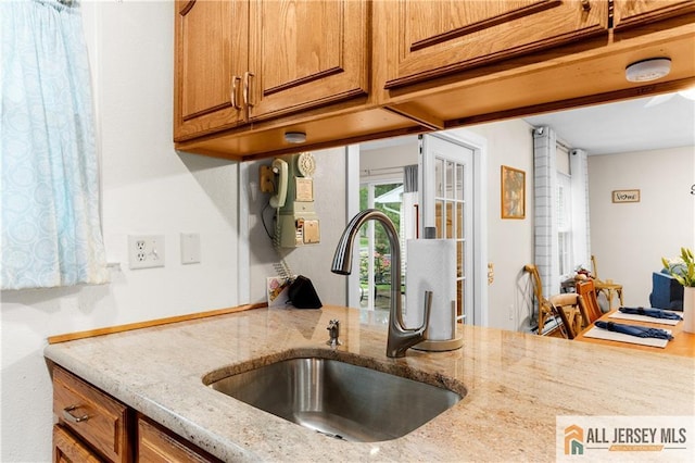 kitchen featuring a sink, brown cabinets, and light stone counters