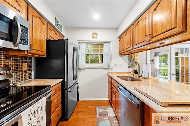 kitchen featuring appliances with stainless steel finishes, a sink, light wood-style flooring, decorative backsplash, and light stone countertops