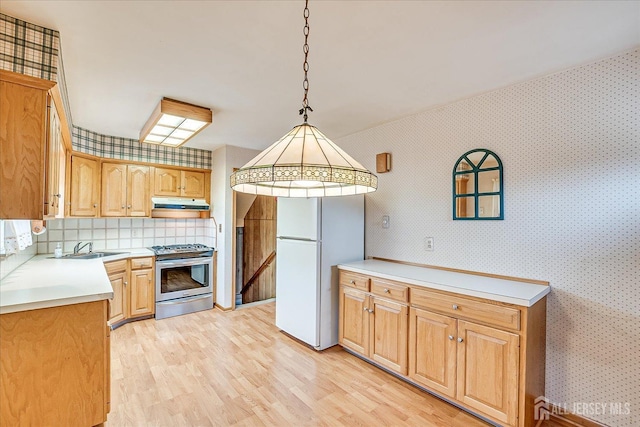 kitchen with pendant lighting, stainless steel stove, sink, white refrigerator, and light wood-type flooring