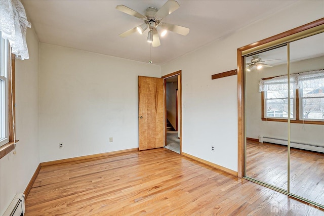 unfurnished bedroom featuring baseboard heating, ceiling fan, a closet, and light wood-type flooring