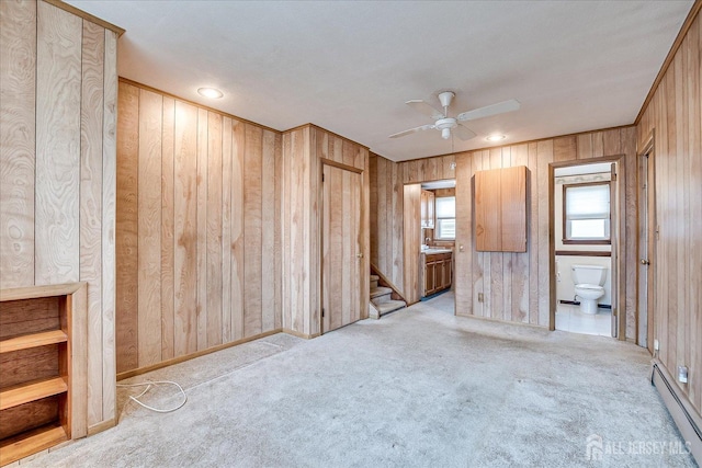 carpeted spare room with ceiling fan, a baseboard radiator, and wood walls