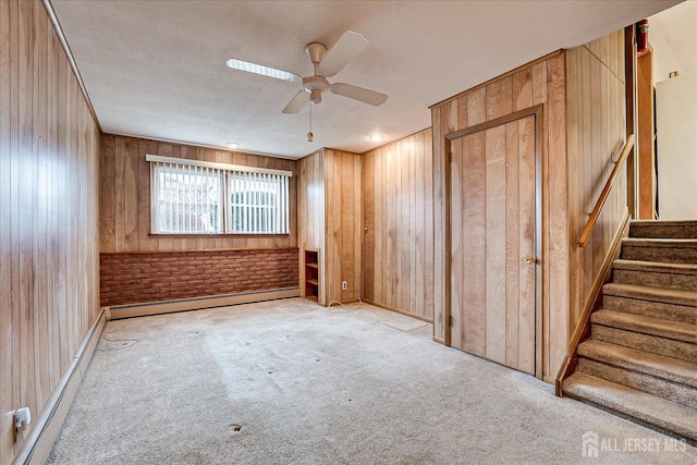 spare room with a baseboard radiator, light colored carpet, ceiling fan, and wooden walls