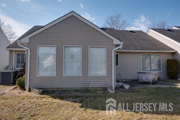 back of property with central AC and a lawn