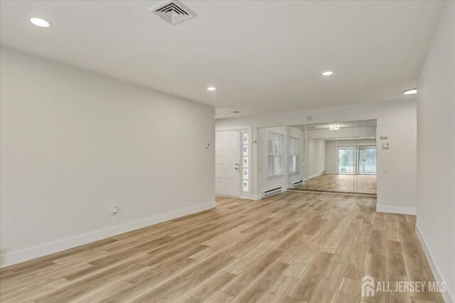 unfurnished living room featuring light wood-type flooring and a baseboard heating unit