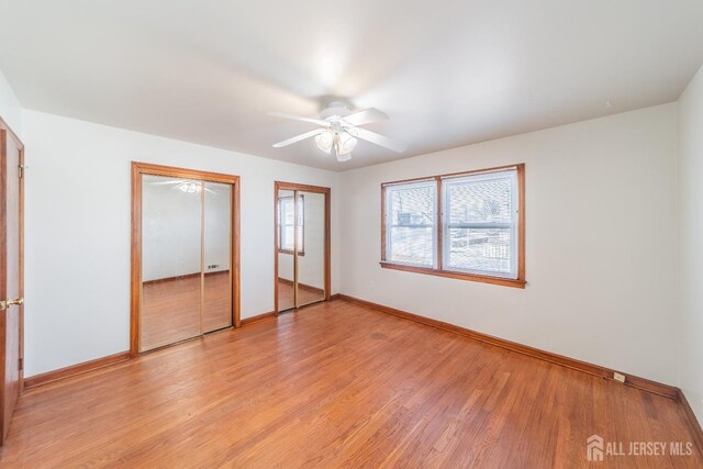 unfurnished bedroom featuring multiple closets, ceiling fan, and light hardwood / wood-style flooring