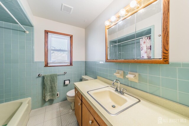 full bathroom featuring tile walls, vanity, shower / bath combination with curtain, tile patterned floors, and toilet