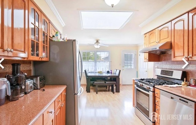 kitchen with stainless steel appliances, under cabinet range hood, ornamental molding, tasteful backsplash, and light stone counters