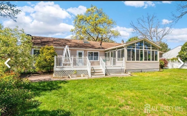 back of property with a sunroom, a wooden deck, and a lawn