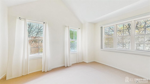 carpeted spare room featuring vaulted ceiling, a wealth of natural light, and baseboards