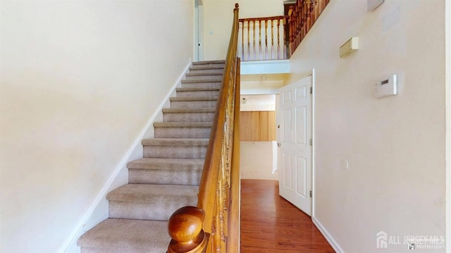 stairs featuring baseboards, wood finished floors, and a towering ceiling