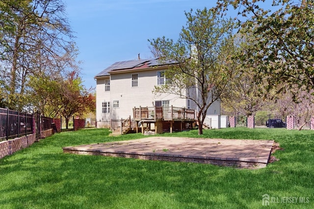 back of house featuring solar panels, fence, a wooden deck, stairs, and a yard