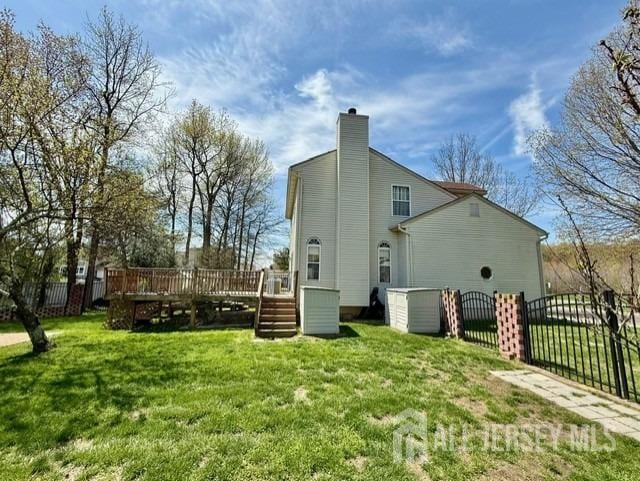 back of property featuring a chimney, fence, a deck, and a yard