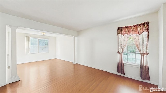 unfurnished room with baseboards, wood finished floors, and a healthy amount of sunlight