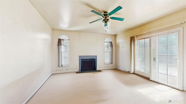 unfurnished living room featuring ceiling fan, baseboards, carpet flooring, and a fireplace with raised hearth