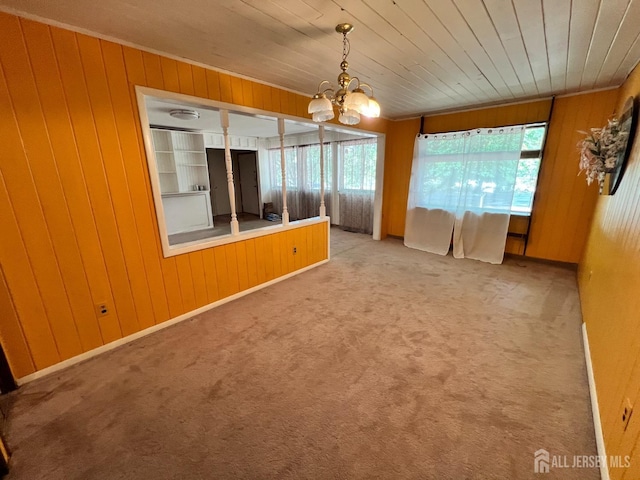 carpeted empty room featuring wooden walls, wood ceiling, and a notable chandelier