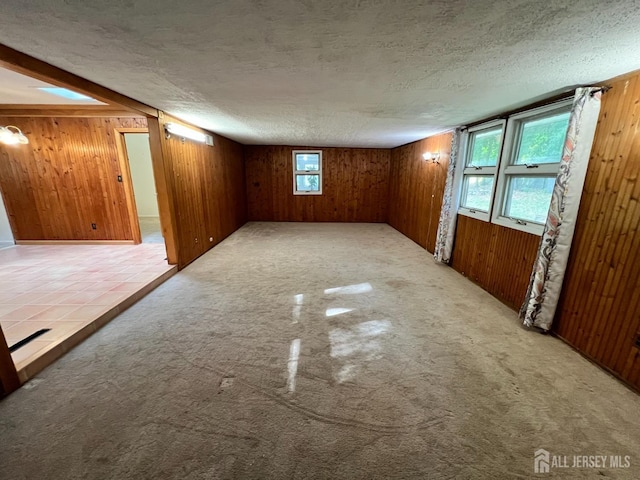 unfurnished room with a textured ceiling, light colored carpet, and wood walls