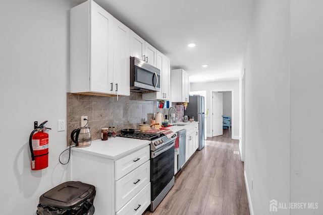 176 Main St, East Brunswick, NJ 08816 - kitchen with appliances with stainless steel finishes, tasteful backsplash, light countertops, light wood-style flooring, and white cabinetry