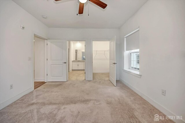 unfurnished bedroom with light carpet, a closet, a spacious closet, and ceiling fan