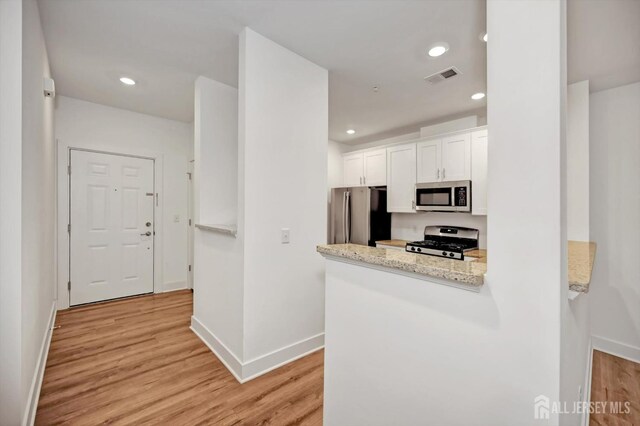 kitchen featuring white cabinetry, light stone counters, light hardwood / wood-style flooring, kitchen peninsula, and appliances with stainless steel finishes