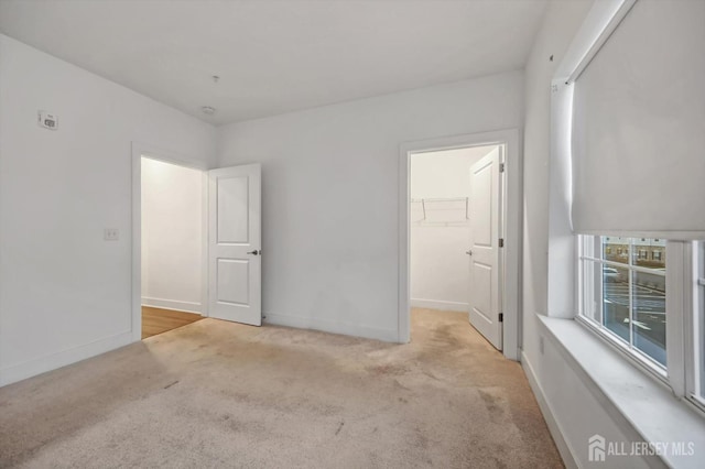 unfurnished bedroom featuring a spacious closet, light carpet, and a closet