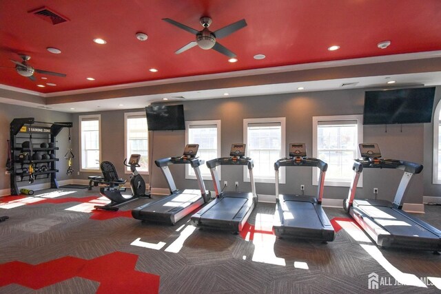 workout area featuring dark colored carpet, ceiling fan, and a tray ceiling