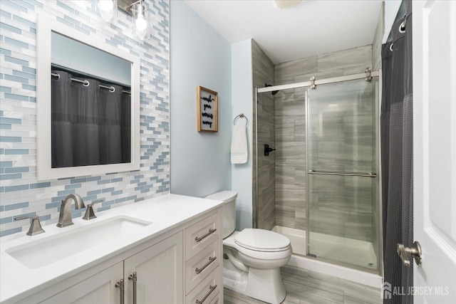 bathroom featuring tasteful backsplash, vanity, a shower with door, and toilet