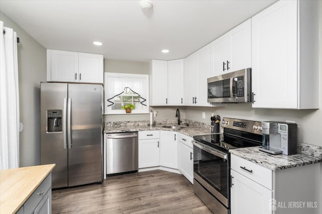 kitchen with dark hardwood / wood-style floors, sink, white cabinets, stainless steel appliances, and light stone countertops