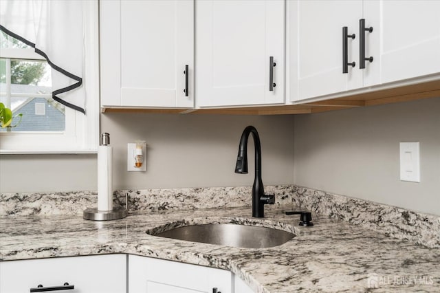 kitchen featuring light stone countertops, sink, and white cabinets