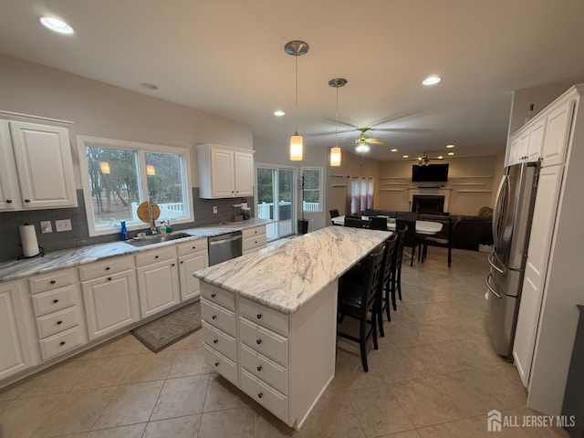 kitchen with stainless steel appliances, a sink, ceiling fan, decorative backsplash, and a breakfast bar area
