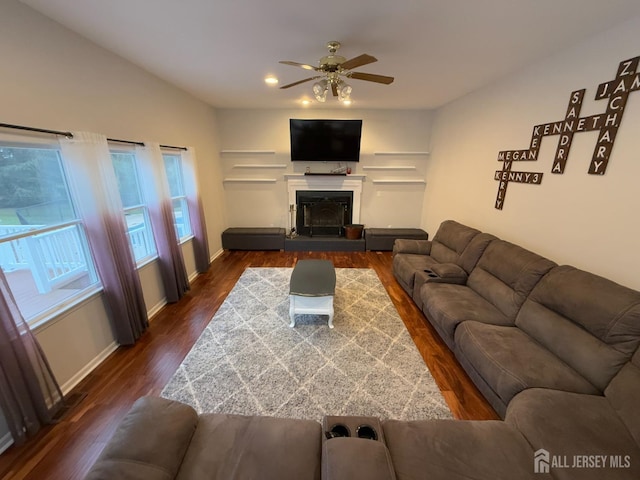living room with a ceiling fan, dark wood-type flooring, baseboards, and a fireplace with raised hearth