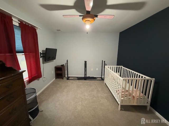 carpeted bedroom with baseboards, a ceiling fan, and a crib